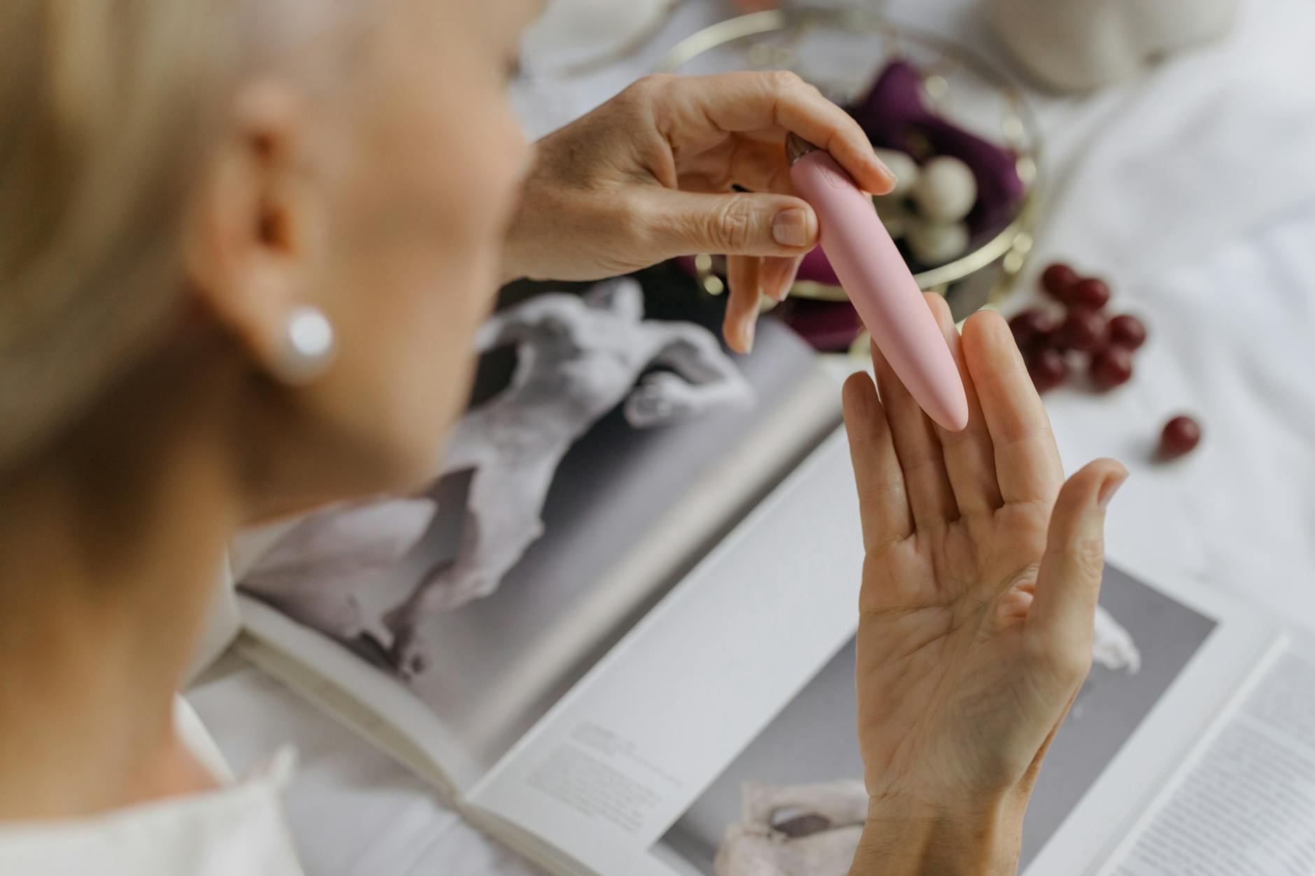 A woman's hands holding a pink vibrator near intimate items, representing postpartum pleasure and self-care.