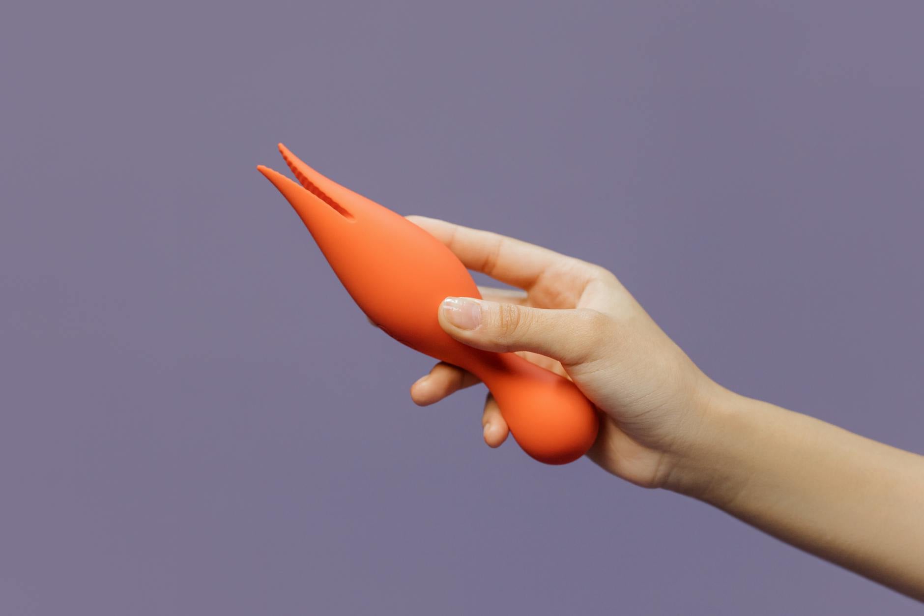 Hand holding an orange lemon-shaped vibrator against a purple backdrop, showcasing modern sensuality and design