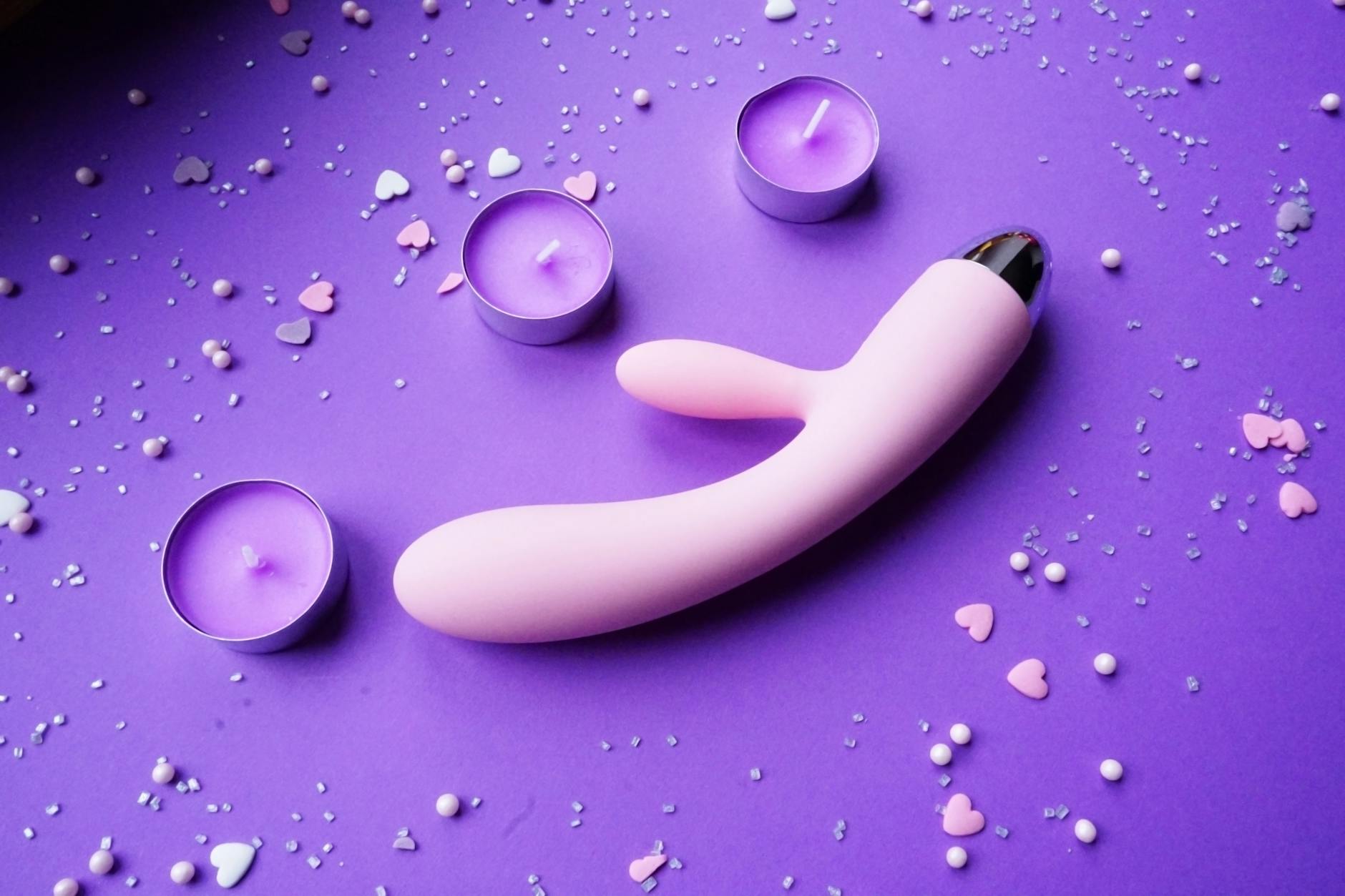Pink vibrator on purple background with heart confetti and candles for romance